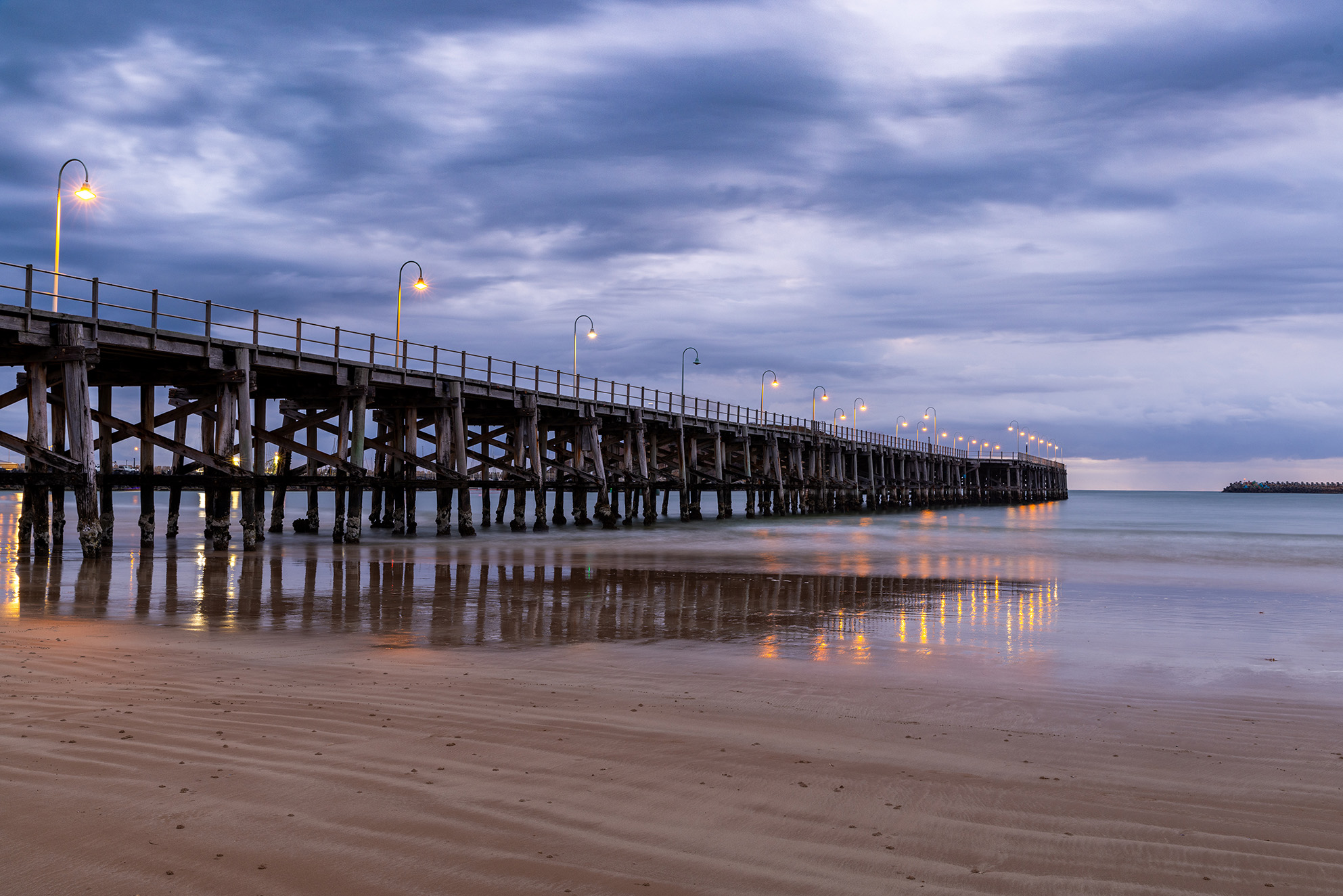 Coffs Harbour jetty at dusk and low tide, cloudy, moody sky and light posts on